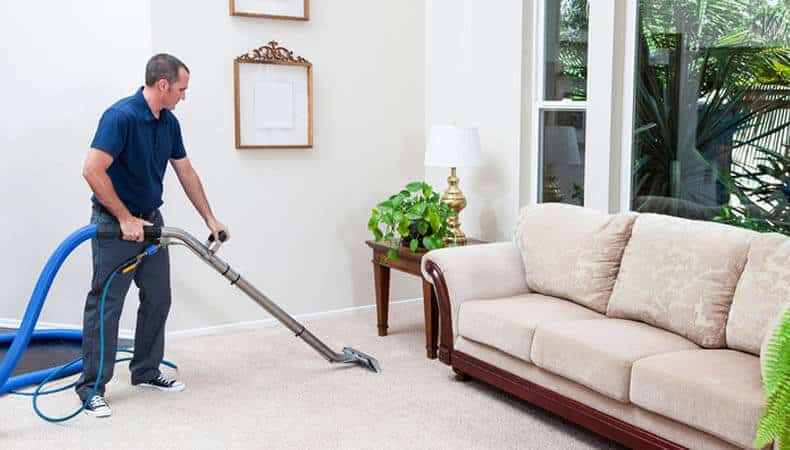This image shows a man using a vacuum to clean a carpet.