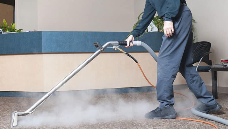 This image shows a man using a steam machine to clean a carpet